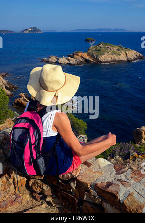 Weibliche Wanderer ruht auf der felsigen Küste von Cap von Estagnol, Fort de Bregancon im Hintergrund, Frankreich, Provence Stockfoto