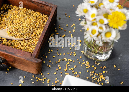 Kleine Holzkiste mit einem Teelöffel Pollen auf eine Schiefertafel mit Blumen, Gänseblümchen und Löwenzahn, auf einer Schiefertafel board Stockfoto