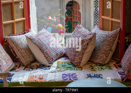 Eine gemütliche Sitzecke in der Nähe der Fenster mit bunten Kissen mit einer wundervollen Aussicht auf den Innenhof in Udaipur, Rajasthan, Indien. Nahaufnahme Stockfoto