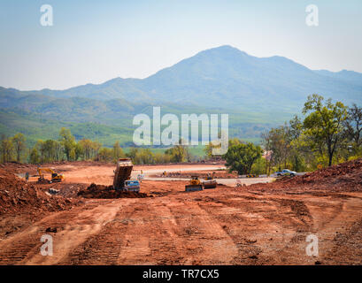 Road Construction Equipment und Road Repair Maschine Graben an der Baustelle mit schweren Tieflöffel Motor Arbeiter am Hang von steilen Berg ba Stockfoto