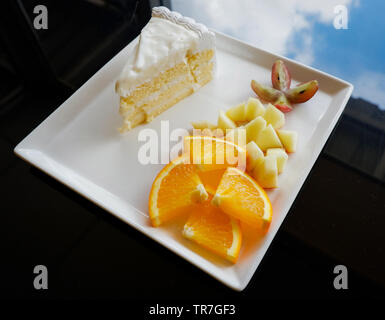 Stück Obst und Milch Kuchen auf weiße Platte/Nahaufnahme von frischen Orange Traube und Apple Slice auf Tablett mit Kuchen sahne Vanille Dessert auf den Tisch Stockfoto