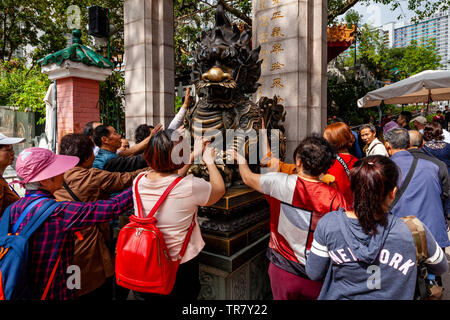 Chinesische Touristen reiben Sie den Drachen Statue für gutes Glück am Eingang zu Wong Tai Sin Tempel, Hongkong, China Stockfoto