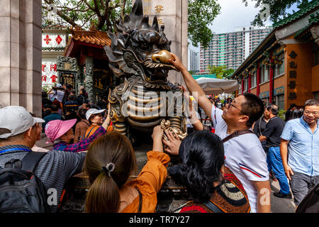 Chinesische Touristen reiben Sie den Drachen Statue für gutes Glück am Eingang zu Wong Tai Sin Tempel, Hongkong, China Stockfoto