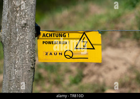 Gelbes Warnschild mit deutschen Wörtern Warnung vor Gefahr und Spannung an einem elektrischen Zaun Stockfoto