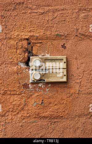 Zwei alte und verschlissene Türklingeln auf eine orange-rote Wand. Stockfoto