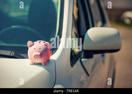 Neues Auto mit pink piggy Bank Geld auf der Motorhaube, im Freien sonnigen Hintergrund. Händler Angebot Credit Finance Services. Auto Leasing, Ankauf Stockfoto