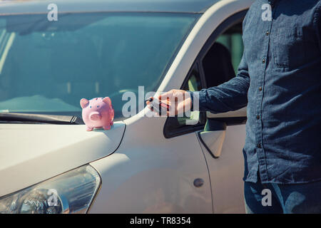 Mann draußen mit seinem neuen Auto Schlüssel und Pink piggy Bank Geld auf der Motorhaube. Händler Angebot Credit Finance Services. Auto Leasing, Fahrzeug günstig online Stockfoto