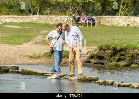 OGMORE VON MEER, WALES - April 2019: Zwei Menschen, die über die Trittsteine über den Fluss Ogwr in Ogmore vom Meer in South Wales. Stockfoto