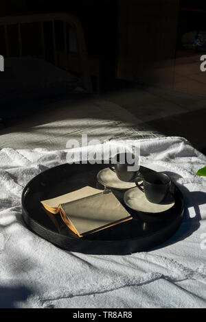 Zwei Tassen und ein Buch auf einem Tablett im Bett - am frühen Morgen Stockfoto