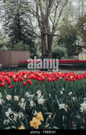 Pella, Iowa, USA - Mai 2, 2019: Skulptur eines niederländischen Frau und zwei Kinder mit einem Korb mit Tulpen in Scholte Gärten. Betten von roten und gelben Tulpen. Stockfoto