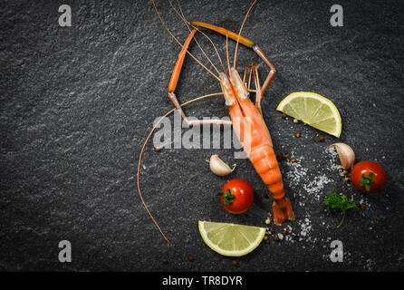 Garnelen Garnelen Gekochte Schalentiere Meeresfrüchte mit Zitronen Tomaten Kräuter und Gewürze auf dunklem Hintergrund Stockfoto