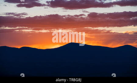 Sonnenuntergang Silhouetten einer Bergkette und färbt den Himmel und Wolken in gelb, orange, lila und rosa - Jemez Bergen in der Nähe von Santa Fe, New Mexico Stockfoto