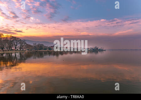Landschaft von Ioannina Stadt erleuchtet von rot, orange Farben Sonnenlicht und glühenden Himmel mit Reflexionen auf der glatten See Wasser. Am späten Nachmittag Szene der See Stockfoto