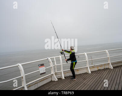 Cromer, Norfolk, Großbritannien. 19. Mai 2019. Ein junger Mann, der einen Köder in der Nordsee beim Fischen am Ende der Pier an einem nebligen Morgen Stockfoto