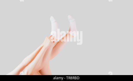 Hand tragen weiße Socken von Menschen auf Grau Studio Light. Seitliche Sicht auf schöne junge Frau tragen helle Baumwolle Socken auf grauen Hintergrund. Stockfoto