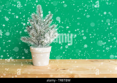 Cute Kiefer in Topf mit Schneefall auf Holz Stehtisch Hintergrund. frohe Weihnachten und Winter Konzepte Ideen. Minimal Style Stockfoto