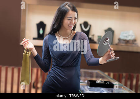 Glückliche junge Frau, die versucht, auf Pearl halskette schmuck shop Stockfoto