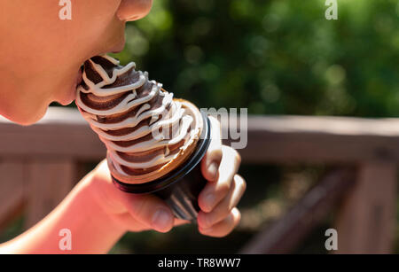 Jungen asiatischen Jungen essen eine Vanille Schokolade kegel Eis, geschossen mit einem seichten dof Stockfoto
