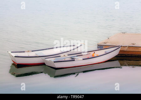 Zwei leere, klein, weiß Ruderboote float Seite an Seite zu einem Pier in Muscongus Bay in Bremen, Maine, USA. Stockfoto