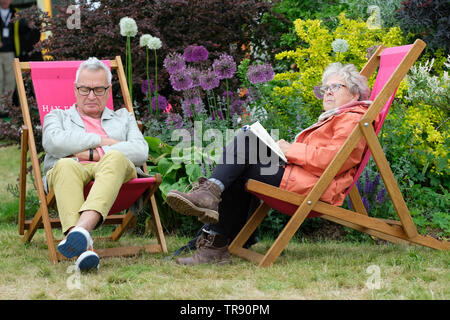 Hay Festival, Heu auf Wye, Powys, Wales, Großbritannien - Freitag, 31. Mai 2019 - ein Besucher wirft ein Auge auf das Wetter als zwei Besucher genießen Sie die Gelegenheit zum Sitzen und in den Liegestühlen auf dem Rasen zwischen den Ereignissen. Foto Steven Mai/Alamy leben Nachrichten Stockfoto