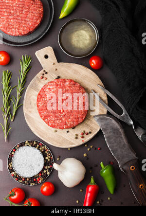 Frisches rohes Hackfleisch hausgemachte Landwirte Grill Beef Burger auf runden Schneidbrett mit Gewürzen und Kräutern und Messer und Gabel auf Braun. Stockfoto