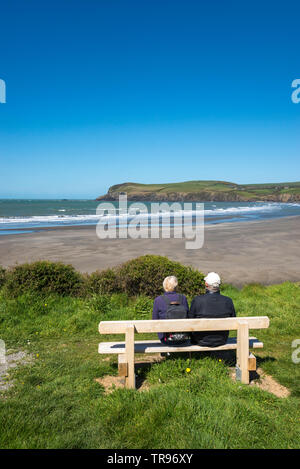 Reifes Paar auf einer Holzbank mit Blick auf Newport Sand an der Küste von Pembrokeshire, Wales. Stockfoto