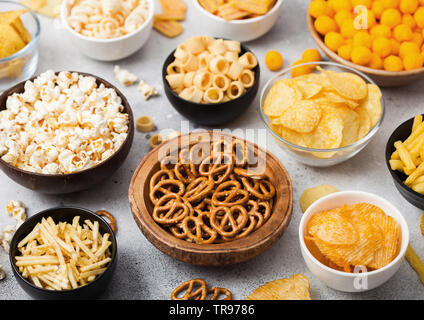 Alle klassischen Kartoffel Snacks mit Erdnüssen, Popcorn und Zwiebelringen und gesalzene Brezeln in Schüssel Platten auf Leuchtkasten. Twirls mit Stöcken und Kartoffelchips Stockfoto