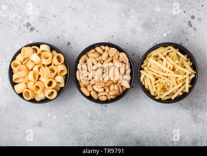 Bereit gesalzen Kartoffel Ringe mit Salz und Essig Sticks und geröstete Erdnüsse als klassische Snack in schwarz Schalen auf hellen Hintergrund. Top View Stockfoto