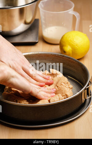 Zwei weiblichen kaukasischen Hände aus den rohen Teig verteilt in einem schwarzen Backblech, backen Geschirr in den Hintergrund - Seitenansicht, Hochformat Stockfoto