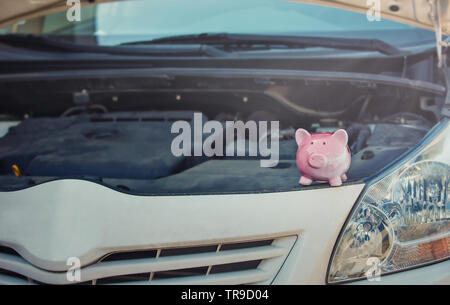 Rosa Schweinchen geld Box auf der geöffneten Haube aus einem kaputten Auto. Finanzielle Anerkennung für Transport Reparatur. Fahrzeug Aufschlüsselung und Investitions conce Stockfoto