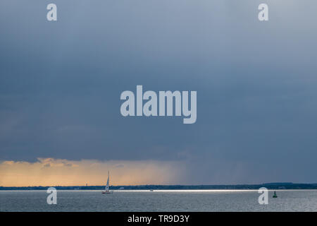 Eine rainfront bewegen sich über Solent mit einsamen single Yacht segeln im Meer mit Boje unter Big Sky Storm clouds orange Sonnenuntergang Stockfoto