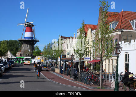 Blick hinunter belebten Straße in Leiden, Niederlande, Molen De Valk, eine historische Windmühle mit der niederländischen Flagge für King's Tag feiern im Jahr 2019 eingerichtet. Stockfoto