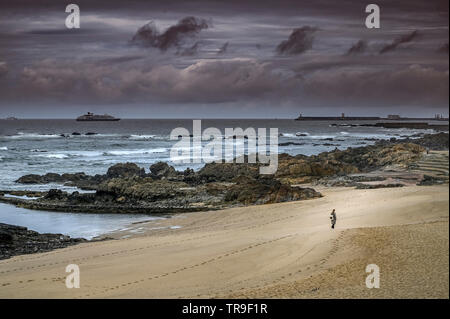 Frau zu Fuß am Strand auf Felsen in Porto ein stürmischer Tag mit dem Hafen und Boote am Horizont Stockfoto