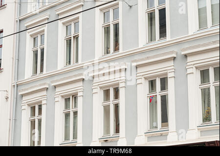 Fassade mit Fenstern auf einem blauen Gebäude. Eine einzelne, kleine norwegische Flagge in einem der Fenster. Stockfoto