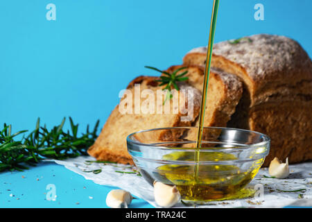 Olivenöl pourin in eine Untertasse Nahaufnahme mit Brot und Kräutern auf bakcground. Mediterrane Küche Konzept. Gesunde Essgewohnheiten. Gvo-frei. Stockfoto