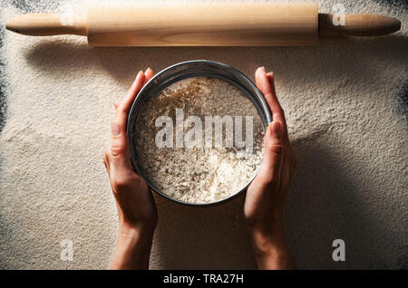 Blick von oben auf die weibliche Hände halten ein Sieb mit Mehl Zubereitung Teig zu machen. Brot Konzept, glutenfreie Ernährung. Stockfoto