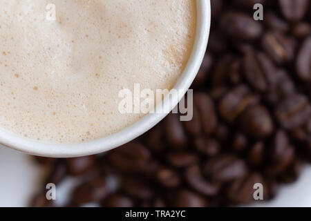 Heißer Kaffee in Papier Cub auf unscharfen rohen Samen Hintergrund, Ansicht von oben Kaffee mit Blasen, Stockfoto