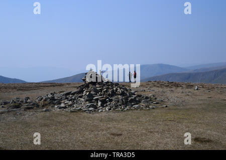 Zwei junge Frauen, die zu Fuß durch die Haufen von Steinen auf dem Gipfel des Wainwright Harter fiel im Nationalpark Lake District, Cumbria, England, Großbritannien Stockfoto