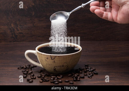 Zucker gießt in Kaffee Tasse mit Kaffee Bohnen auf Holz- Hintergrund Stockfoto