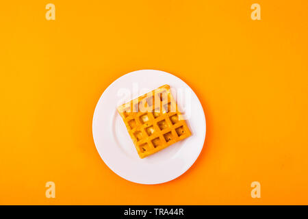 Knusprige square Belgische Waffel auf einer weißen Platte auf einem gelben Hintergrund. Ansicht von oben, flach Stockfoto