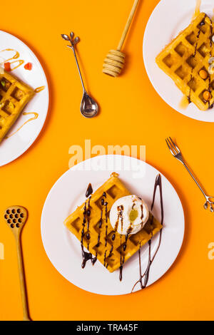 Frische Golden Square Belgische Waffeln auf Platten mit Eis und Belag auf einem gelben Hintergrund. Ansicht von oben, flach Stockfoto