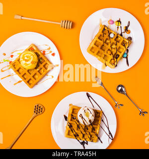 Frische Golden Square Belgische Waffeln auf Platten mit Eis und Belag auf einem gelben Hintergrund. Ansicht von oben, flach Stockfoto