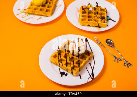Frische Golden Square Belgische Waffeln auf Platten mit Eis und Belag auf einem gelben Hintergrund Stockfoto