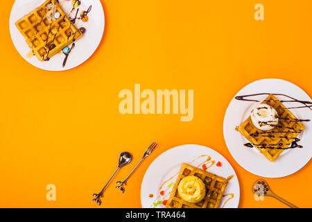 Frische Golden Square Belgische Waffeln auf Platten mit Eis und Belag auf einem gelben Hintergrund. Ansicht von oben, flach. Platz kopieren Stockfoto