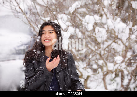Biracial jugendlich Mädchen tragen schwarze Lederjacke, außerhalb im Winter während starker Schneefall, genießen das Wetter Stockfoto