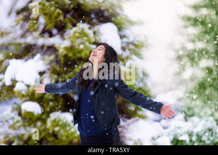 Biracial jugendlich Mädchen tragen schwarze Lederjacke im Winter Schneesturm, ausgestreckten Armen und Gesicht in Richtung Himmel, genießen Schneeflocken f Stockfoto