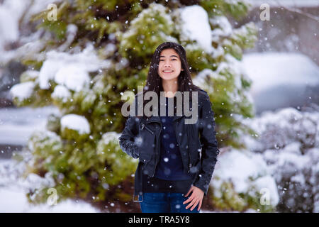 Biracial jugendlich Mädchen tragen schwarze Lederjacke, außerhalb im Winter während starker Schneefall, genießen das Wetter Stockfoto