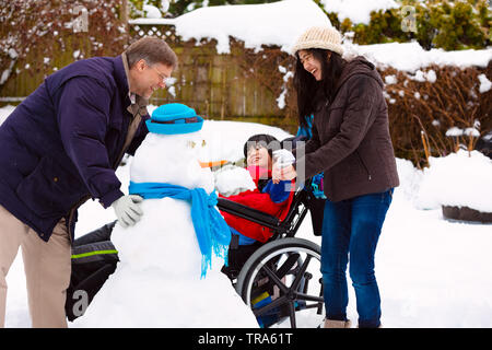 Deaktiviert biracial Junge im Rollstuhl einen Schneemann bauen mit Vater und Schwester im Winter nach Schneefall Stockfoto