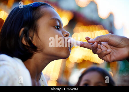 Süße kleine asiatische Mädchen lecken Finger ihrer Mutter, die Zuckerwatte auf Es hat Stockfoto