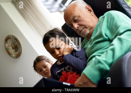 Kaukasische Großvater sitzt mit seinen beiden Grand Kinder im Wohnzimmer spielen auf einem mobilen Gerät zusammen Gaming Stockfoto